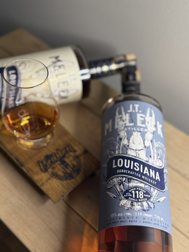 JT Meleck 100% rice whiskey 96 proof bottle and 118 proof bottle lying on side angled around glencairn and the bourbon bishop wooden tasting board