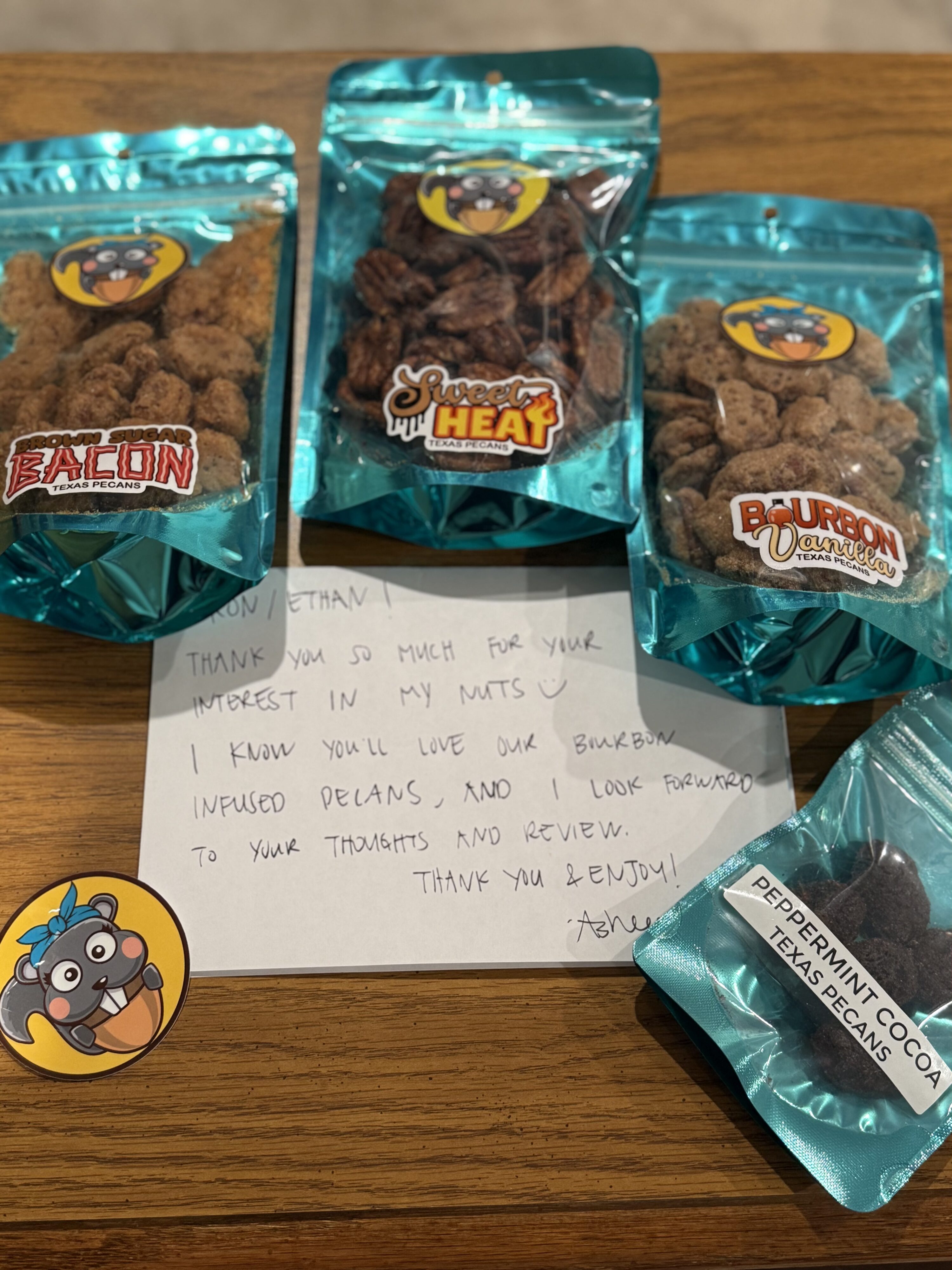 Aw, Nuts Texas Pecans in various flavors with handwritten note centered on desk and Aw, Nuts logo sticker to side