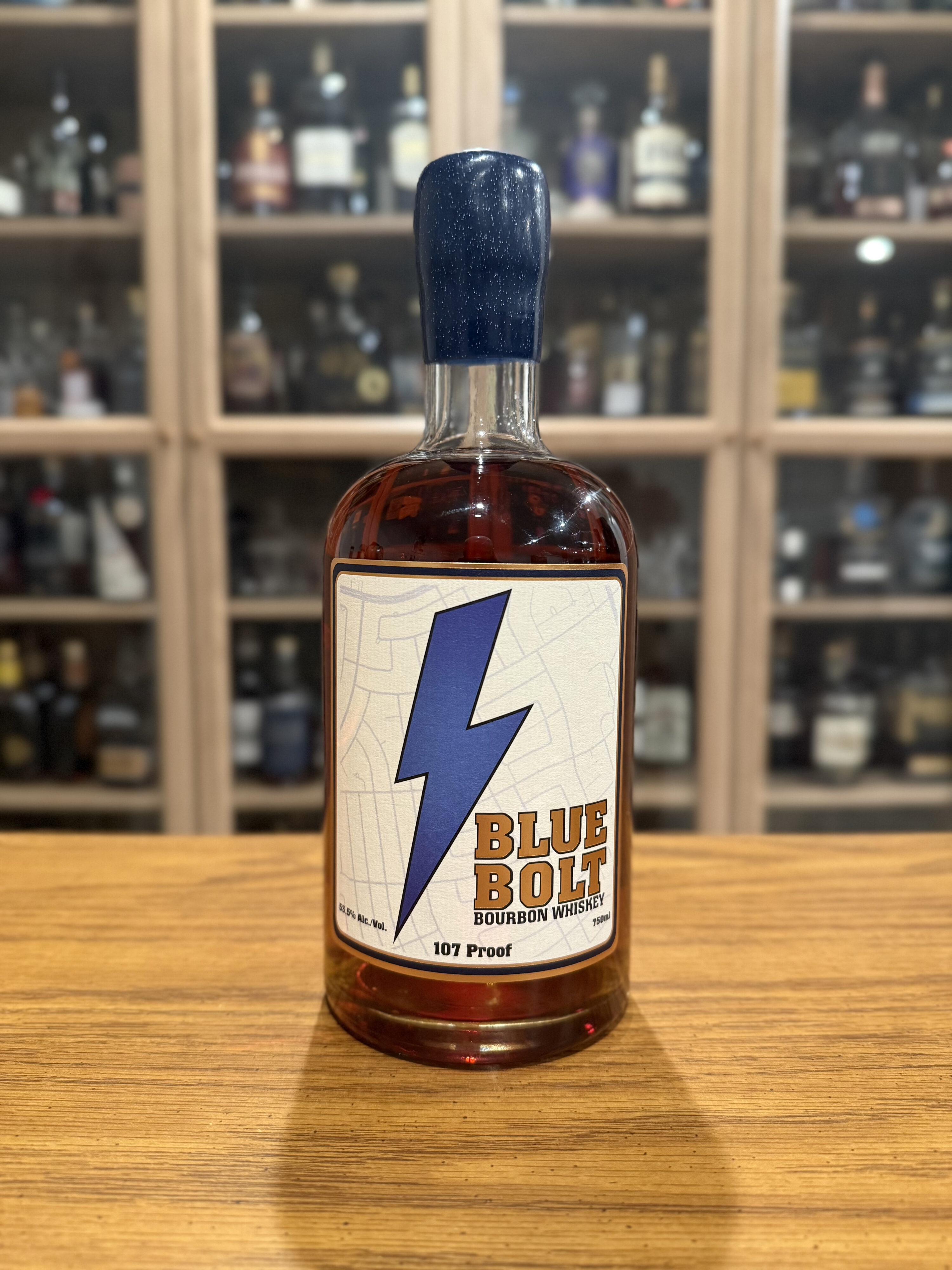Blue Bolt 107 Proof Small Batch Bourbon on desk in front of whiskey collection