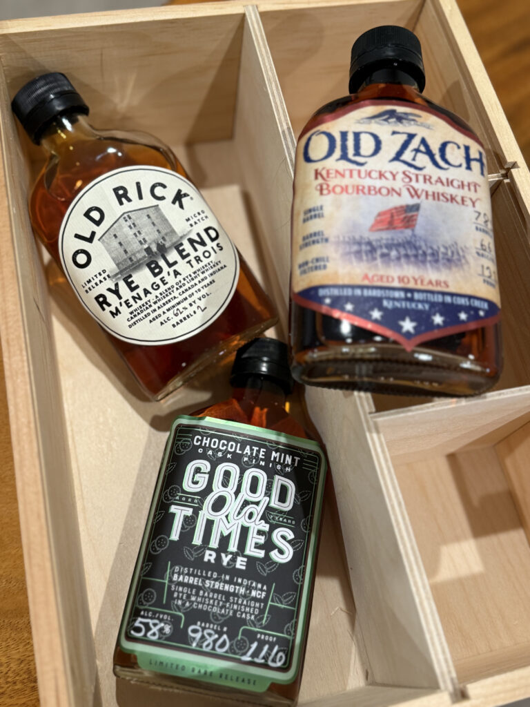 Good Times Chocolate Mint Cask Finished Rye 116 Proof and Old Rick Menage A Trois Rye Blend 124 Proof visible with blurred sample from Old Zach on box