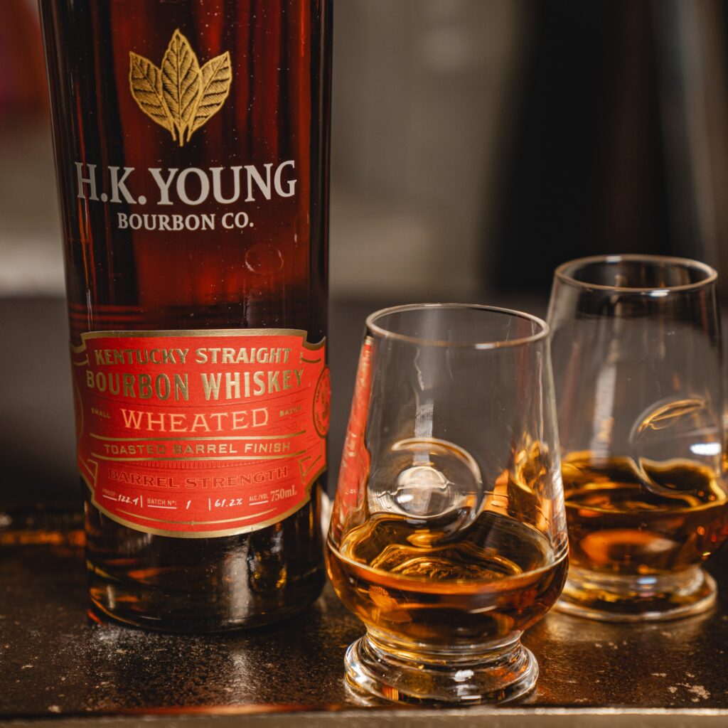 Close up of H.K. Young Toasted Wheated Bourbon Barrel Strength on tray beside two full glasses.