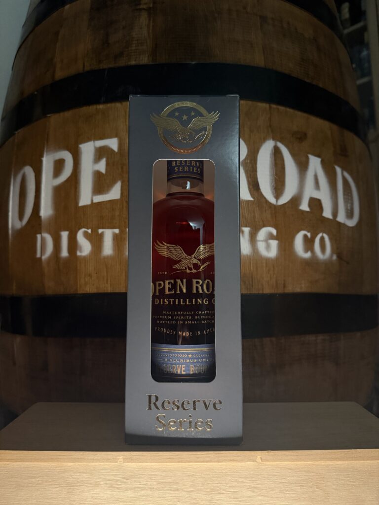 Open Road Reserve Bourbon in box standing in front of Open Road whiskey barrel