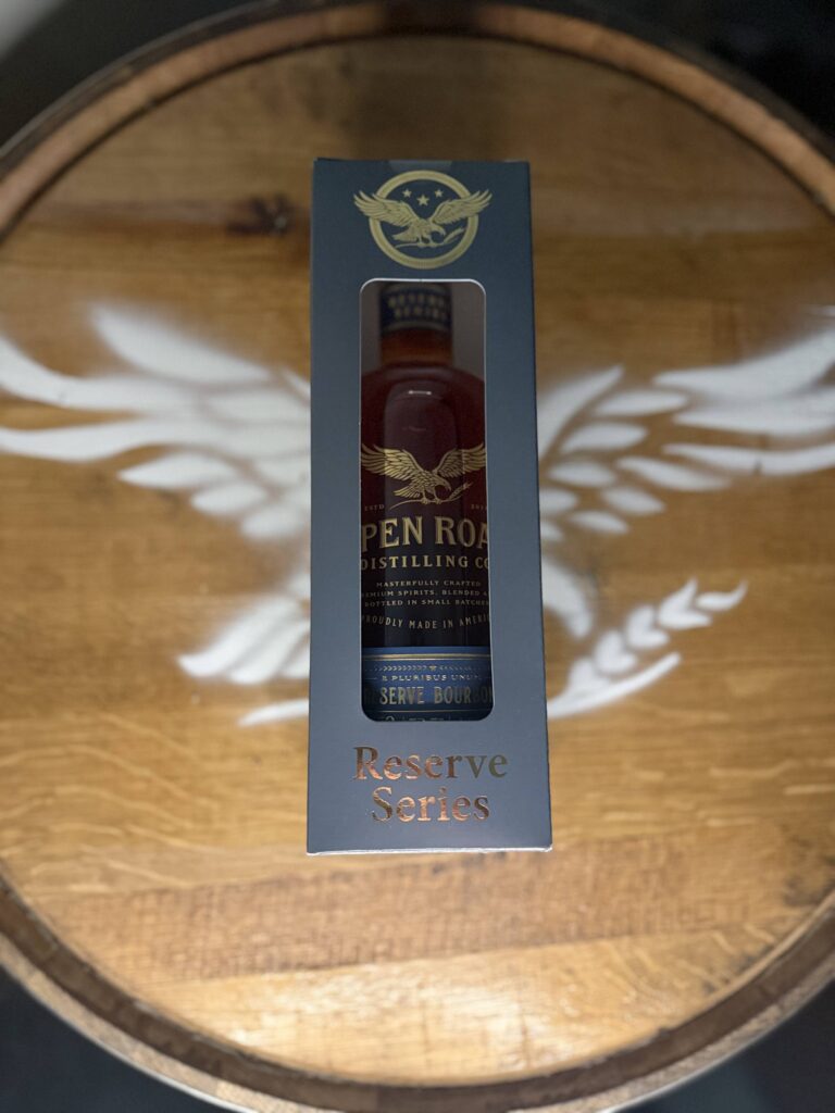 Open Road Reserve Bourbon in box lying centered over Open Road eagle logo on whiskey barrel head