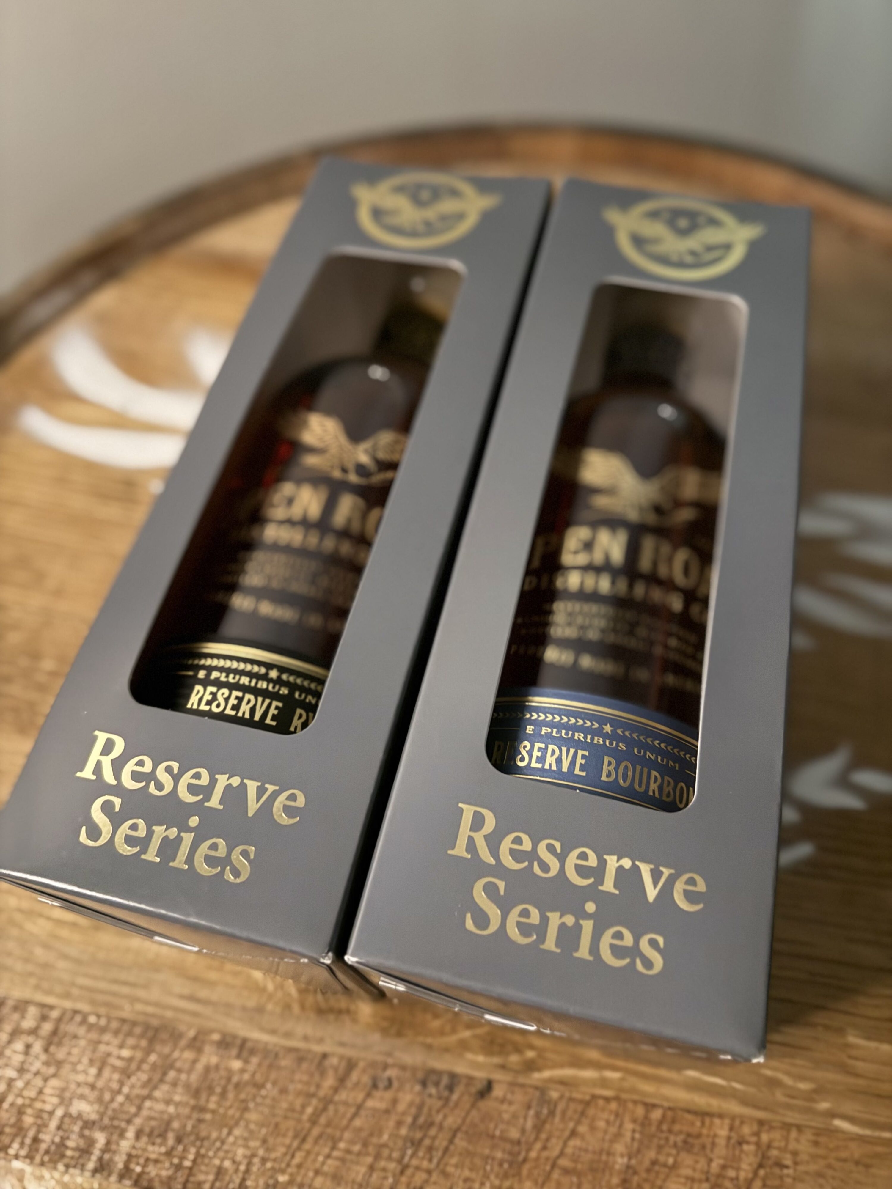 Open Road Reserve Rye and Bourbon in box lying on side over Open Road eagle logo on whiskey barrel head