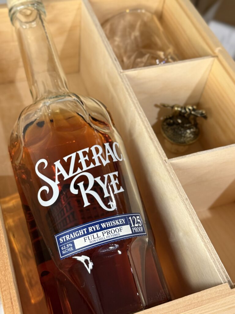 Sazerac Full Proof Rye lying in wooden gift box with glass and blantons topper side view