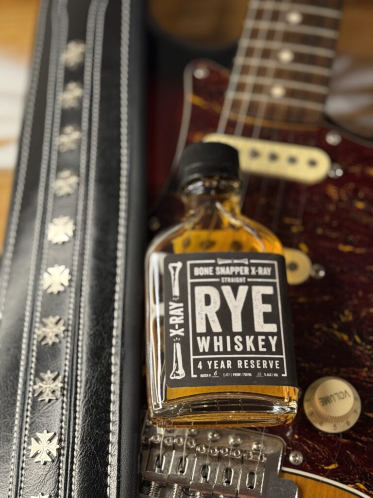 Backbone x-ray bonesnapper rye lying on guitar body next to studded guitar strap