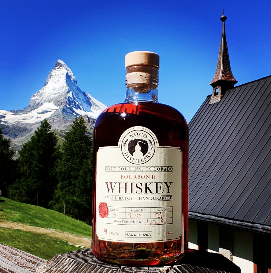 Noco Distillery Bourbon ll Sanguis Christi posed in front of mountains and steeple taken by dearwhisky.com