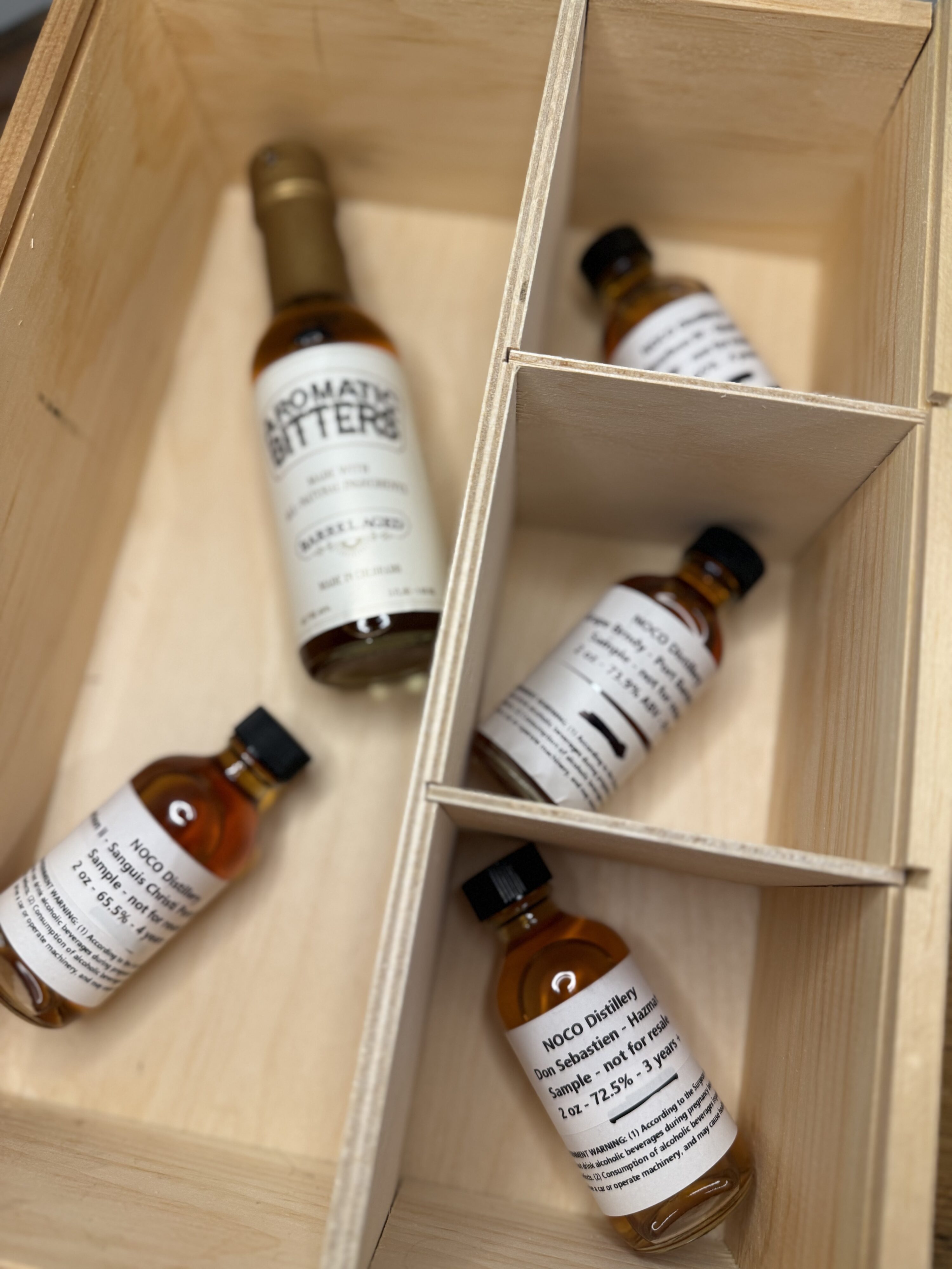Noco Distillery four spirit samples and aromatic bitters on desk in wooden box but blurred
