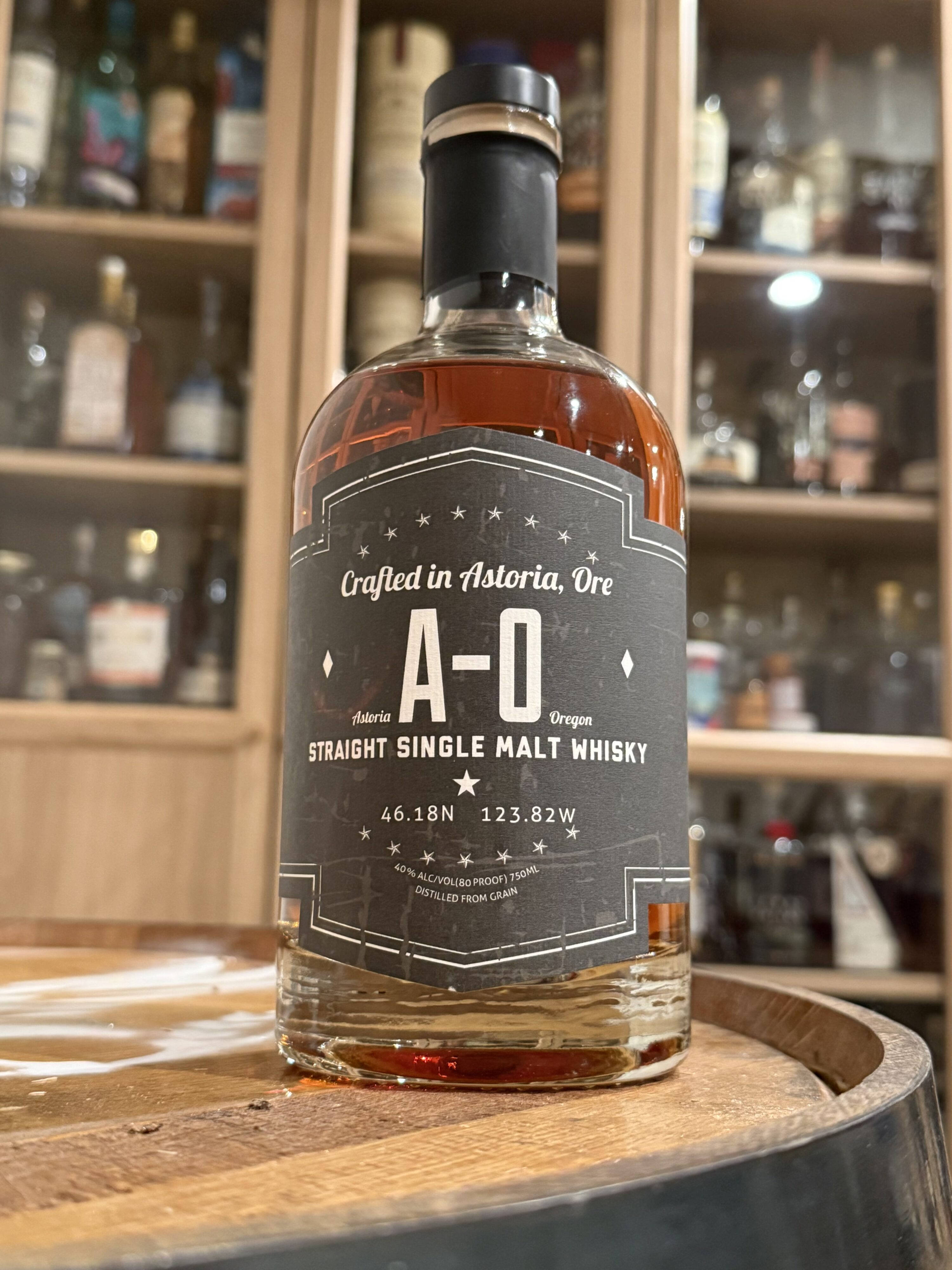 Pilot House A-O Single Malt Whiskey sitting on whiskey barrel in front of whiskey collection