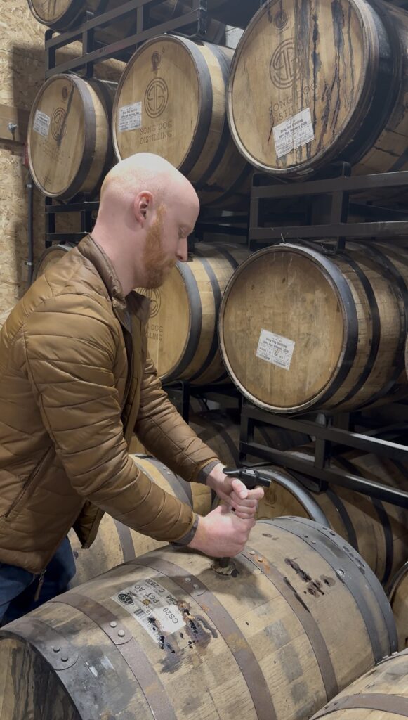 E.S. Pope pulling bung from Song Dog rye whiskey barrels