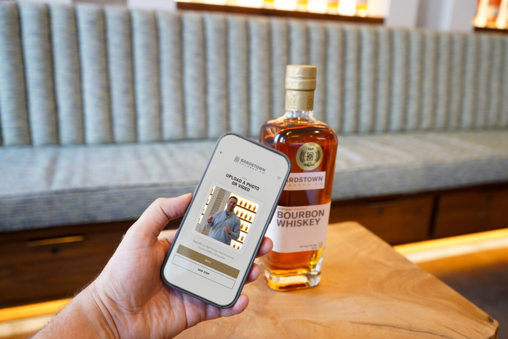 Phone app shown in front of Bardstown Bourbon Company bottle with NFC tag on it