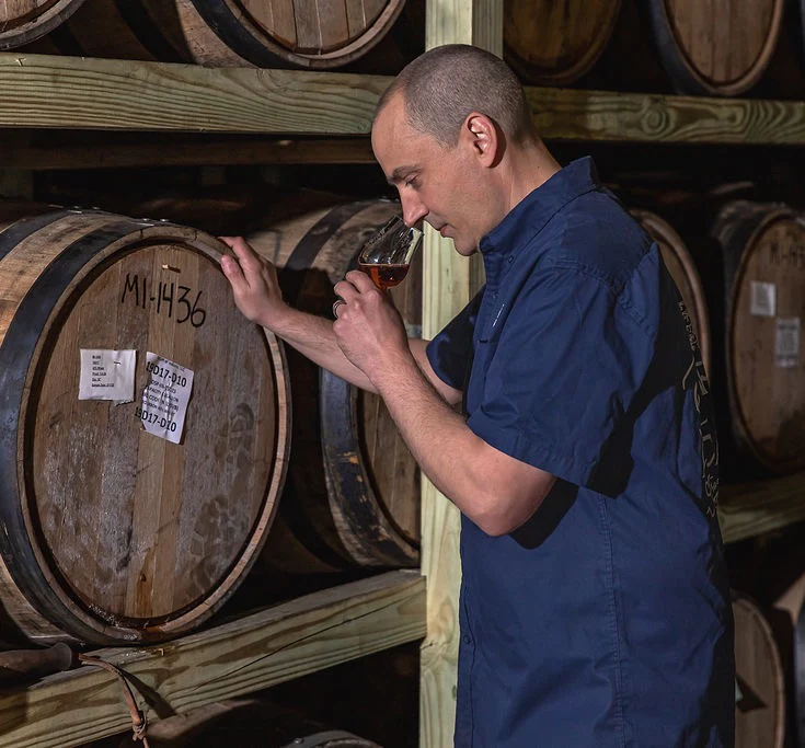 Copper & Cask's "Barrel Master" Stephen Corrigan nosing a glass of whiskey beside whiskey barrels.