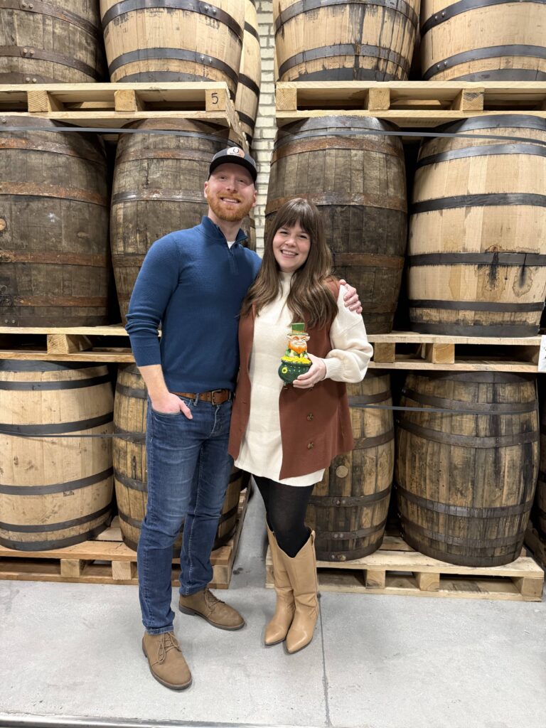 E.S. Pope & his wife Jessica posing in front of rum barrels with leprechaun statue