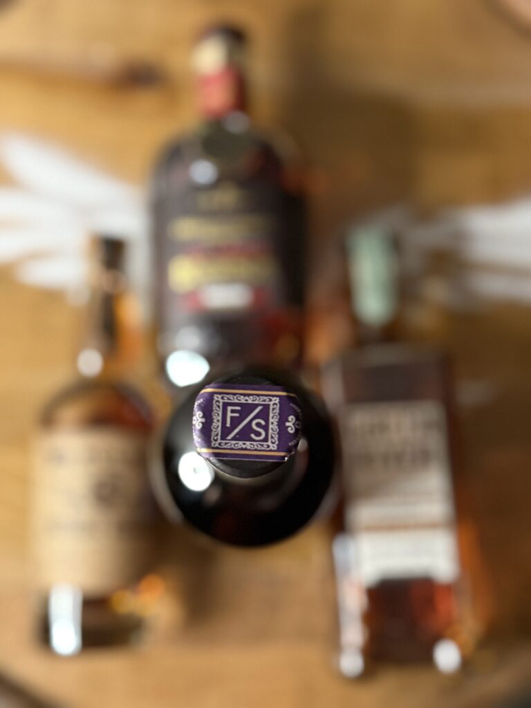 Forward Slash Quintessium topper over blurred sourced distillery bottles