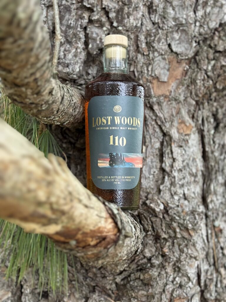 Lost Woods 110 Proof Cask Strength ASM nestled in branches of tree against wide trunk