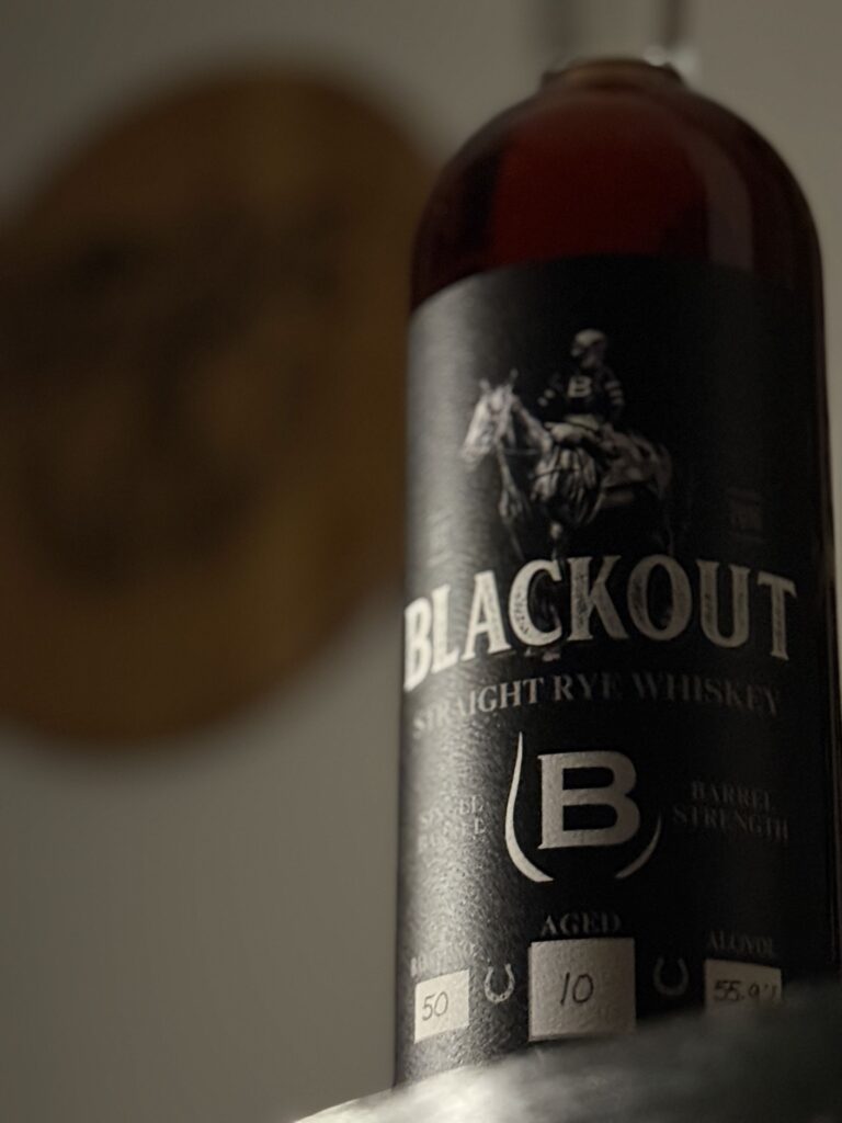 Blackout 10 Year Cask Strength Single Barrel Rye off-center with blurred bourbon bishop barrel head behind it.
