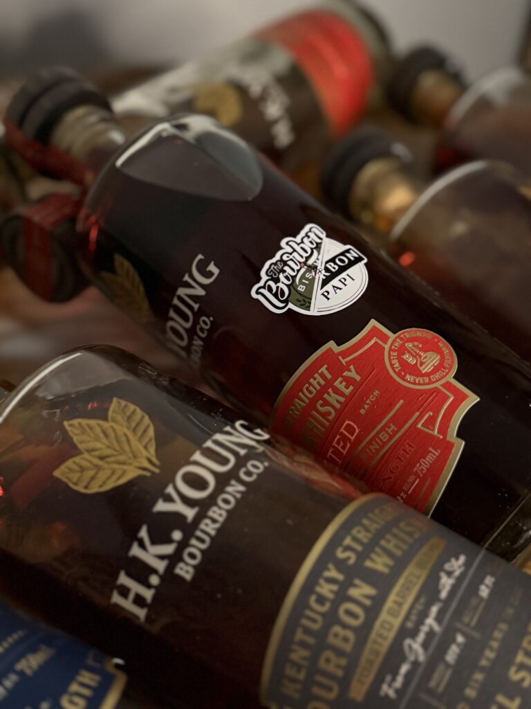 H.K. Young "The Bourbon Bishop x Bourbon Papi" Toasted Wheated Bourbon Single Barrel from side, lying in collection of other H.K. Young releases