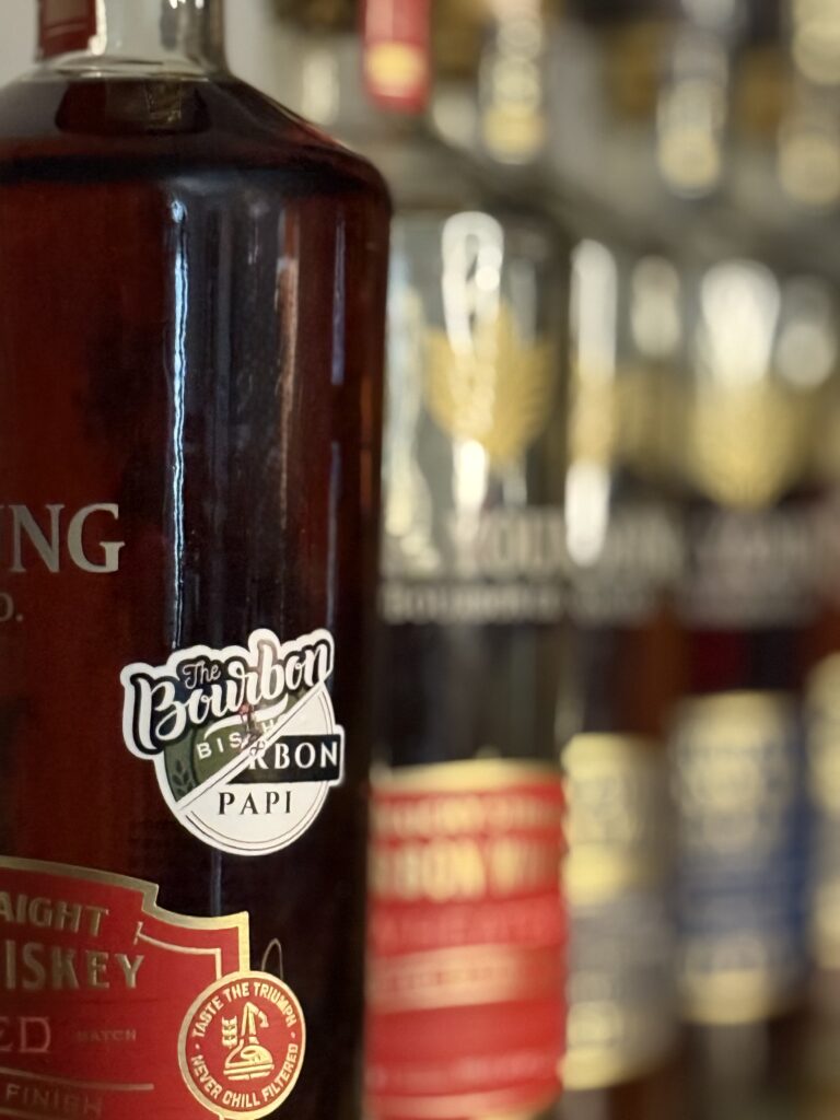 H.K. Young "The Bourbon Bishop x Bourbon Papi" Toasted Wheated Bourbon Single Barrel sticker with unfocused line of previous H.K. Young picks beyond it