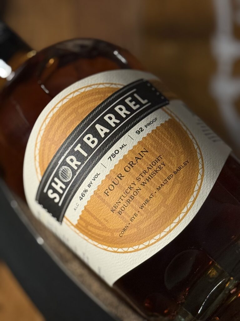 Shortbarrel Four Grain Bourbon lying on whiskey barrel