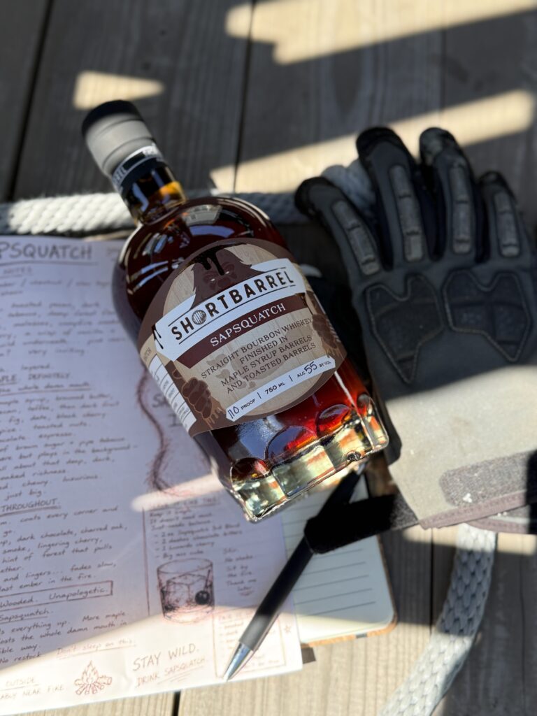 Shortbarrel Sapsquatch Maple-Finished Bourbon 2026 Release lying on "sapsquatch" notes beside gloves