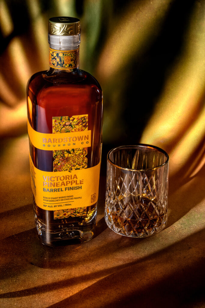 Bardstown Bourbon Company's new Victoria Pineapple Rum finished whiskey and full glass against glowing sunshine esque background