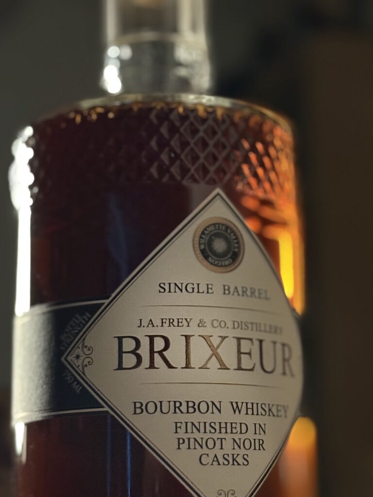 Brixeur Spirits Triple Wine Finished Bourbon backlit on whiskey barrel close-up