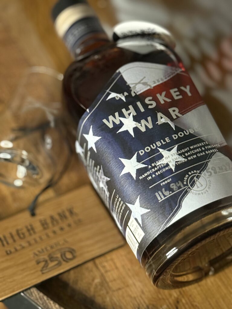High Banks Whiskey War Double Double Oak 250th Anniversary Release lying beside blurred whiskey war glass and wooden tag