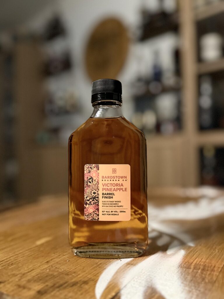 Bardstown Bourbon Company Victoria Pineapple sample standing on whiskey barrel in front of collection