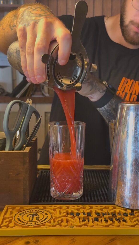 Bartender Joey pours blackberry cocktail from shaker into glass