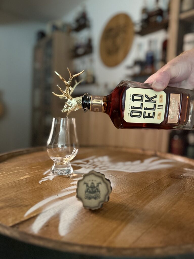 Old Elk 10-Year Wheat Whiskey pouring from golden elk head spout into glencairn