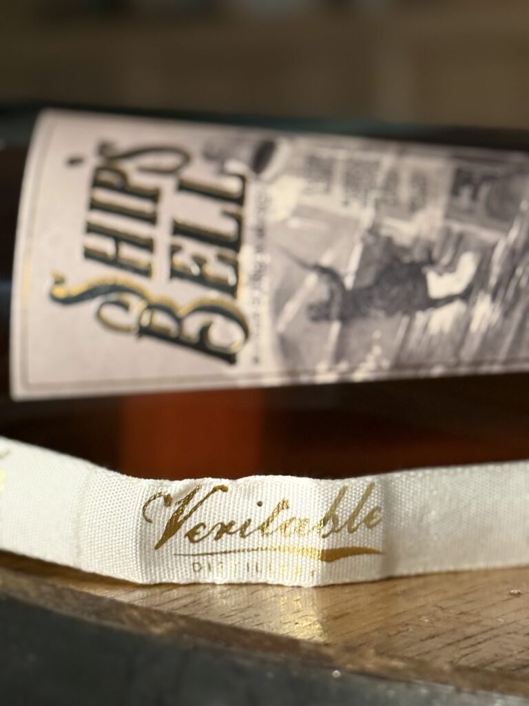 Veritable "Ships Bell" blended bourbon lying on side with ribbon in front