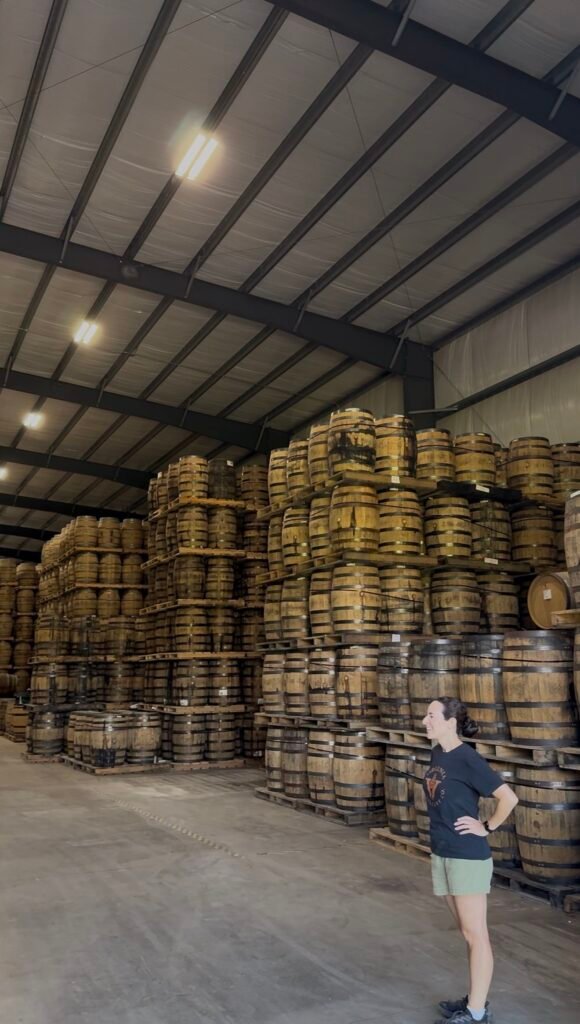 VDC's Director of Liquid Development and Lead Blender Amanda Beckwith smiles towards barrels in cask house #1