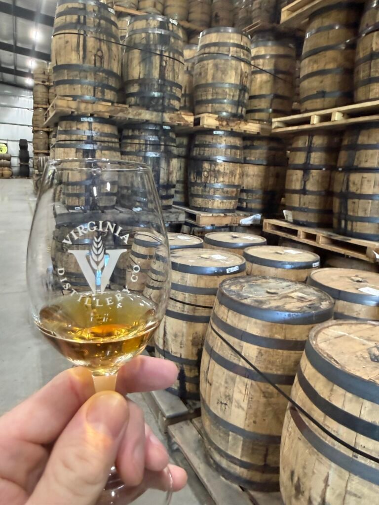 Glass full of STR ASM in front of cask house #1 barrels