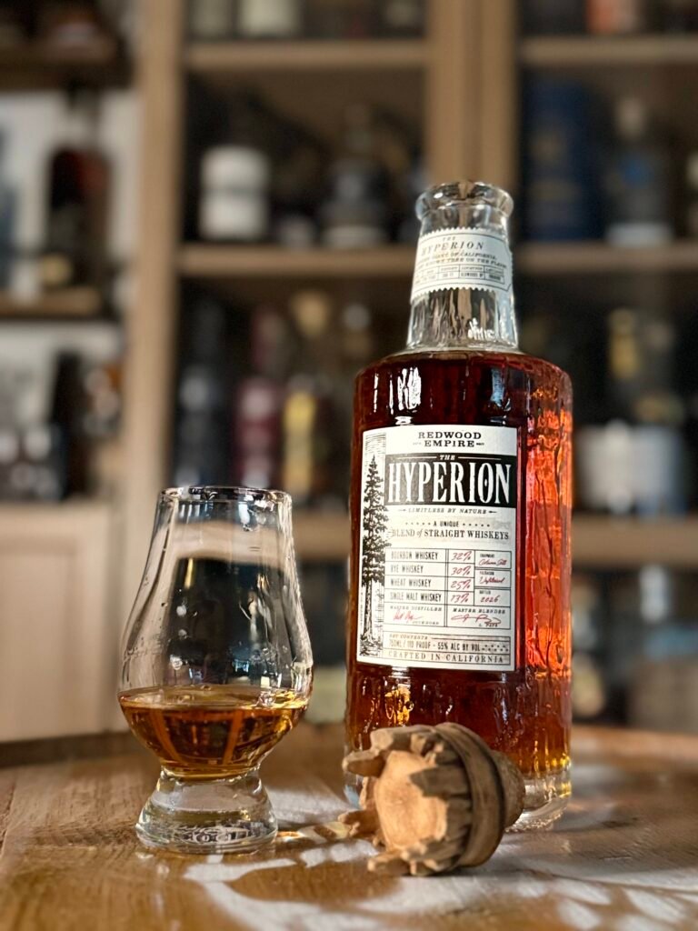 Redwood Empire The Hyperion whiskey open on whiskey barrel with crown like topper beside full glencairn