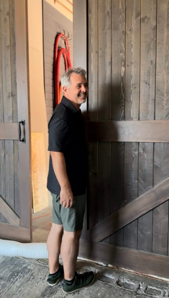 Dave smiles, talking back to Nick, as he opens the barn doors into the distillation room