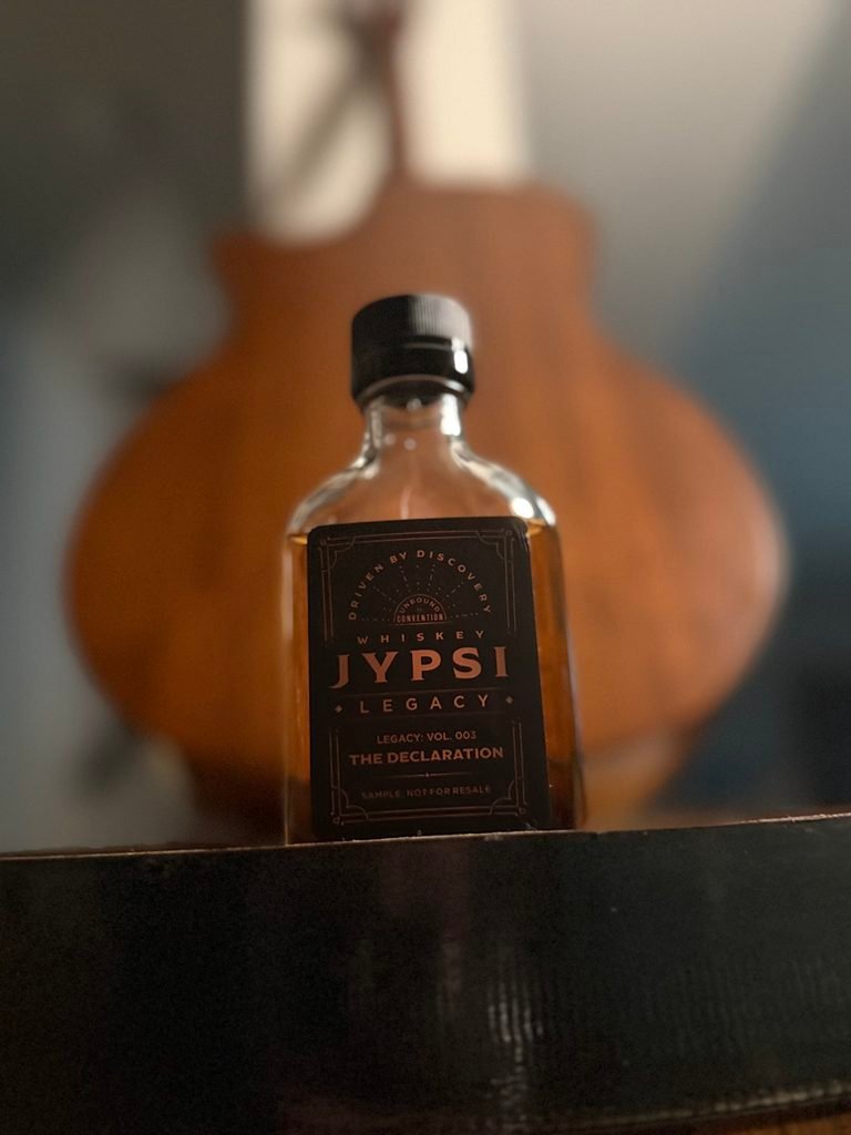 Whiskey JYPSI Legacy Batch 003 "The Declaration" stands on barrel with back of guitar behind it