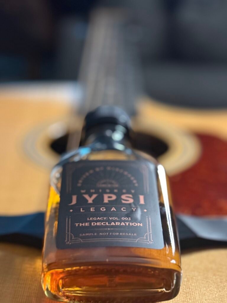 Whiskey JYPSI Legacy Batch 003 "The Declaration" lies flat on guitar strings with guitar blurred