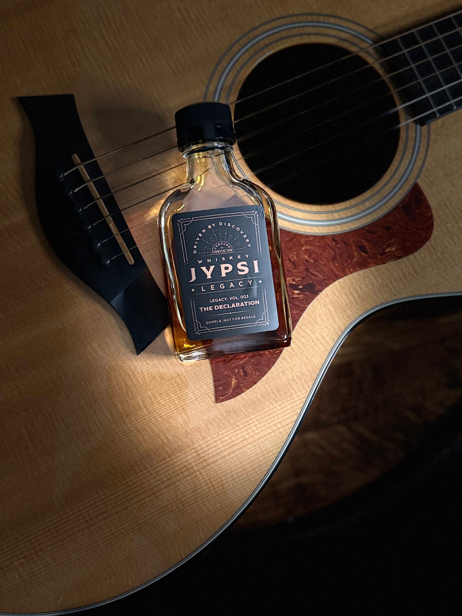 Whiskey JYPSI Legacy Batch 003 "The Declaration) lays spotlighted across guitar front